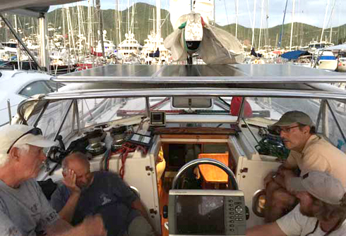 Captain Thom Burns, foreground left, conducts crew debrief after practice and races to help with familiarization to boat and avoiding mistakes. Owner, Captain Dale Soumis with hand on head, Tim Giesen, and Jacques Soumis, foreground right. Note the second set of solar panels. Dragonsbane had not been connected to shore power in over a year!